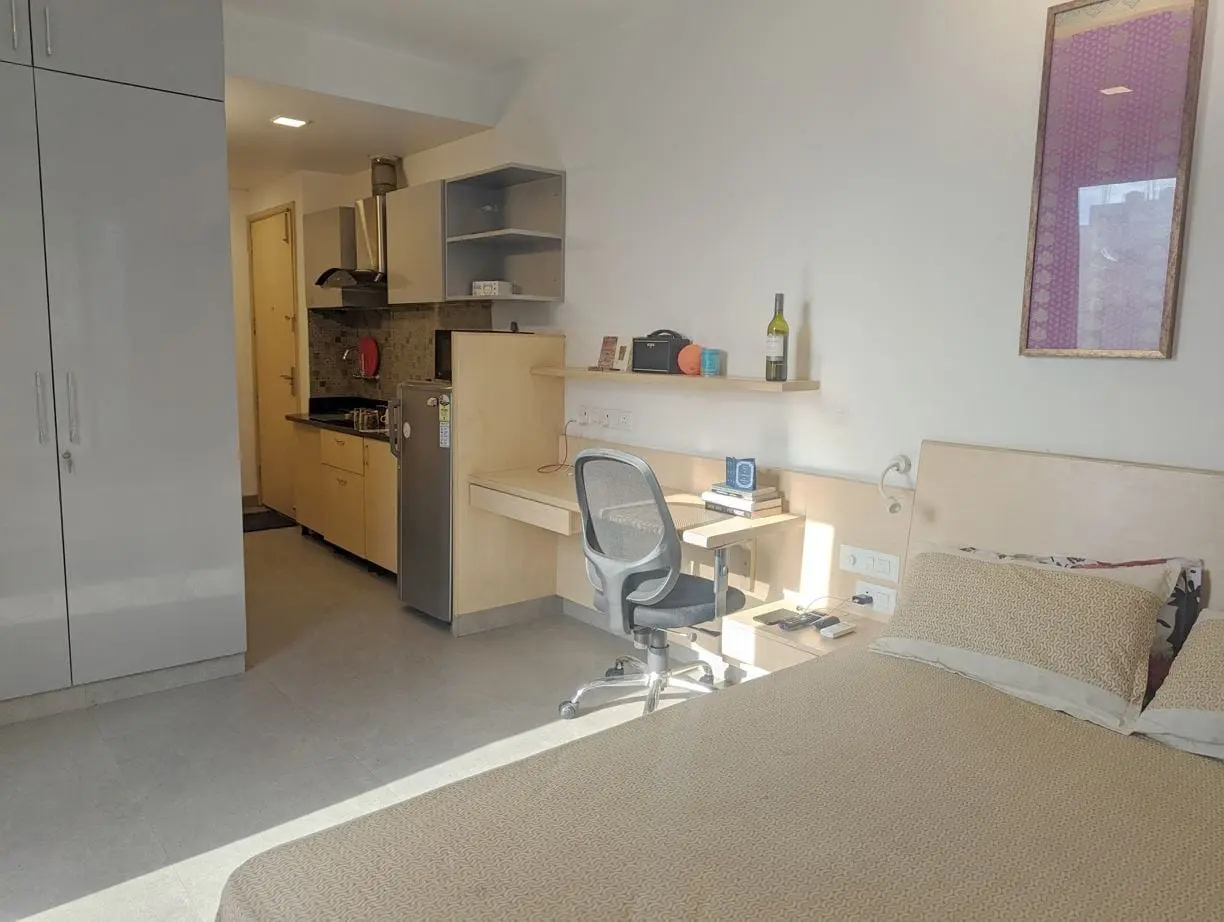 A sunlit Commune Prime studio with bed, work desk, wardrobe and kitchen pantry