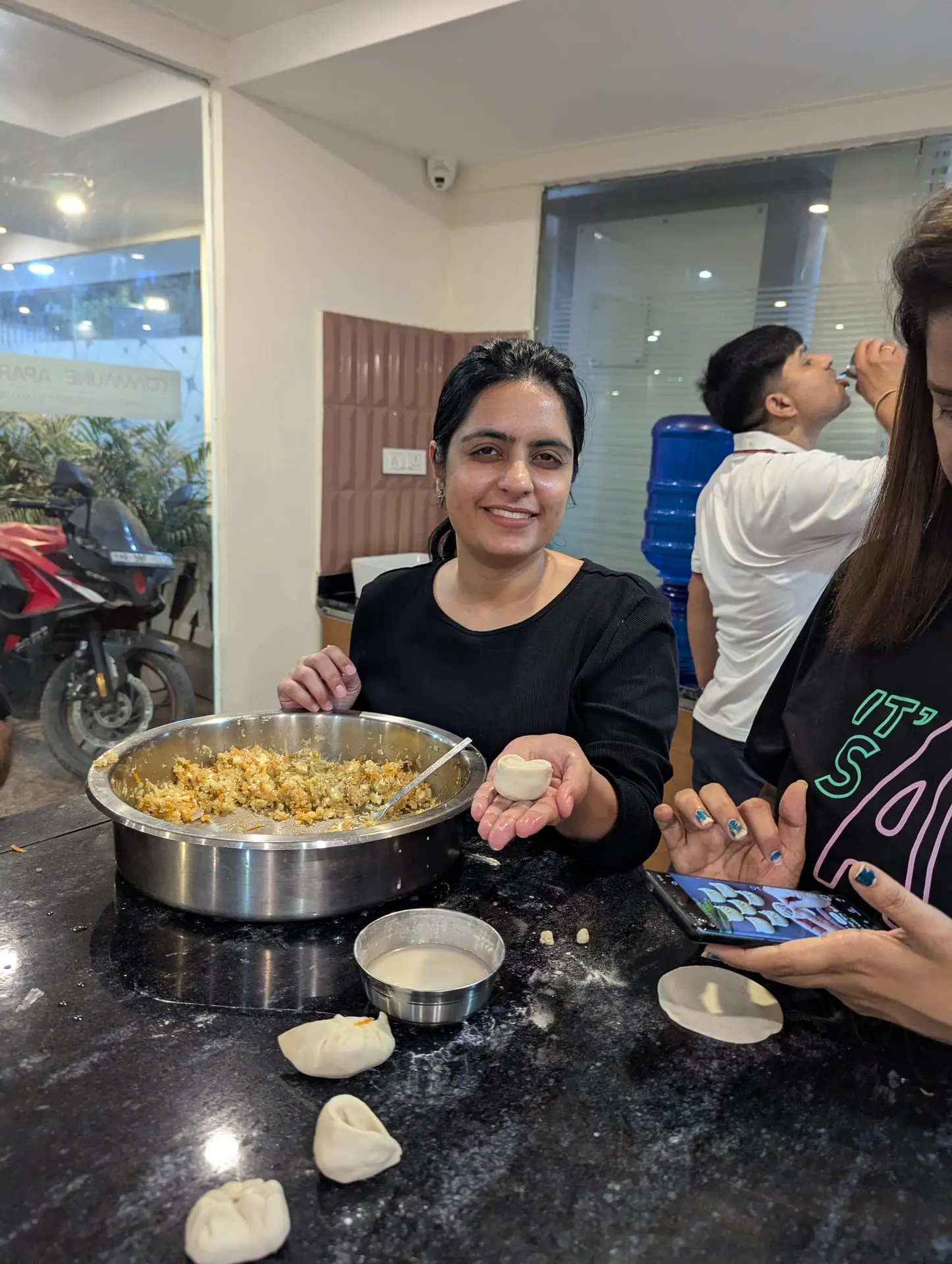 A Communr smiling while pleating a momo over a bowl of filling
