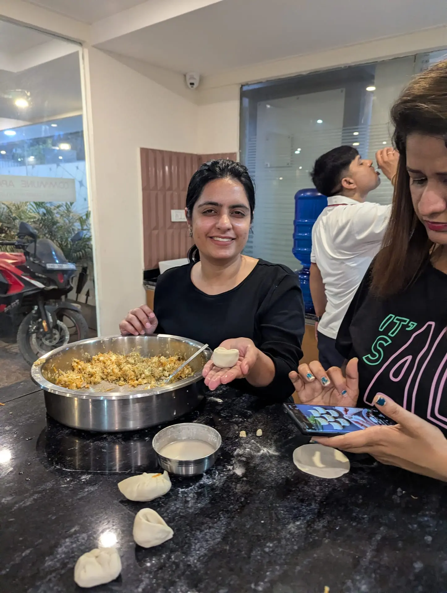 A Communr pleating a momo, with dough and filling laid out in the community kitchen