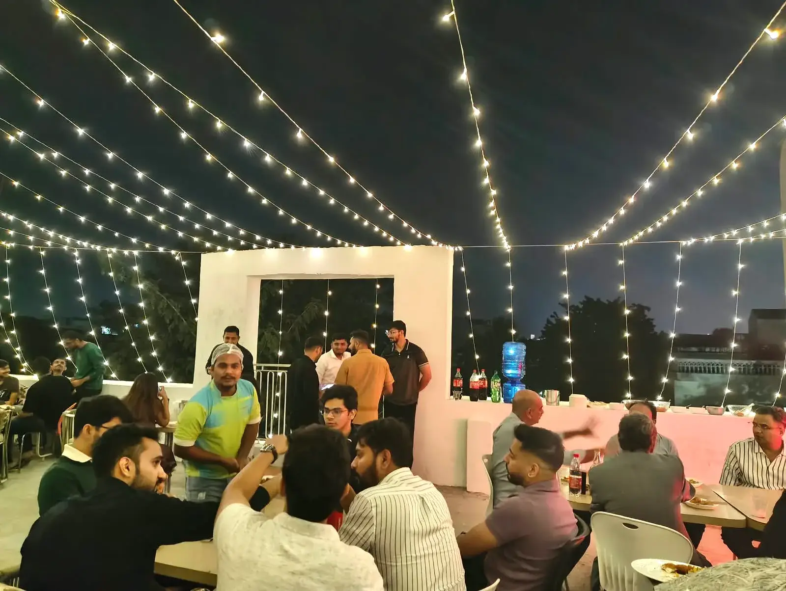 The rooftop lit end to end with string lights, tables crowded underneath
