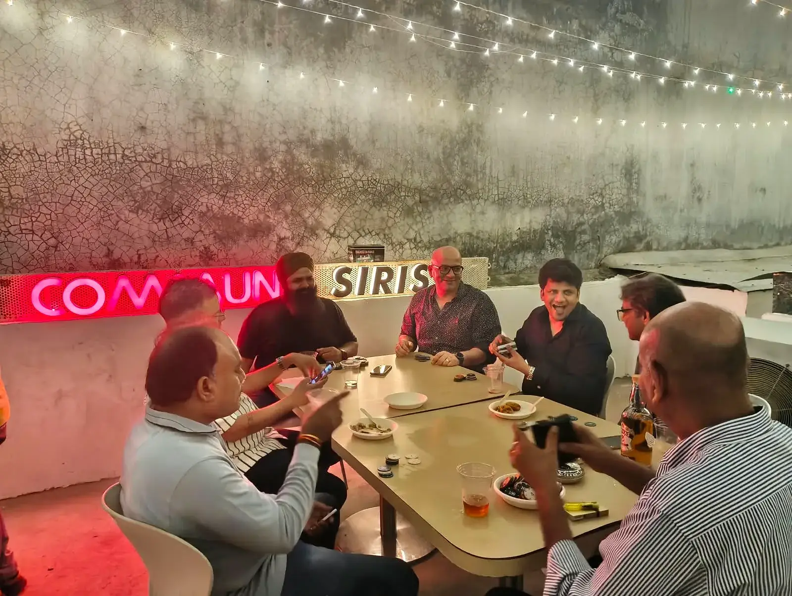 Communrs around a table beside the neon Commune Siris sign