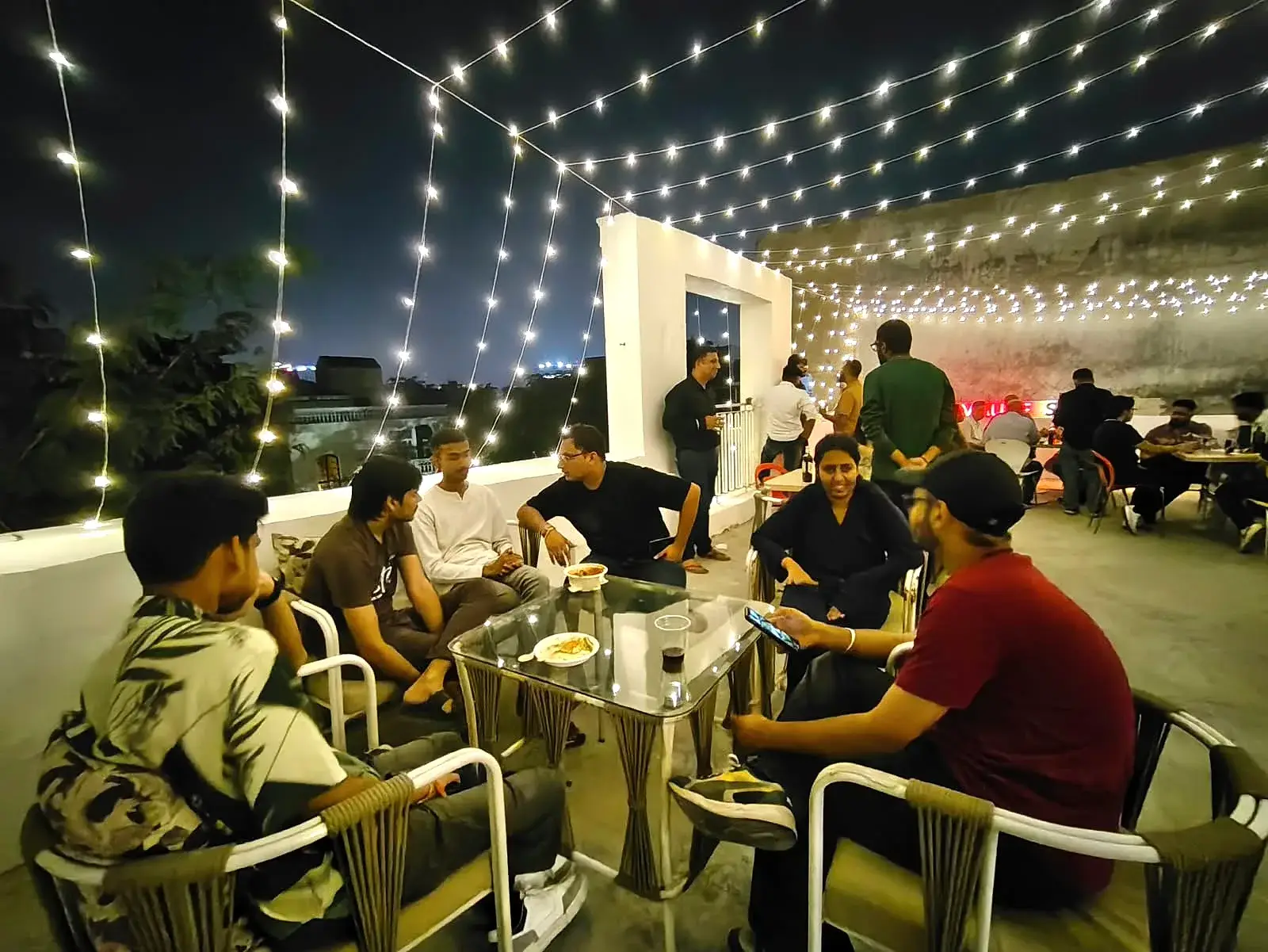 Communrs sitting in groups across the rooftop, the Gurugram skyline behind