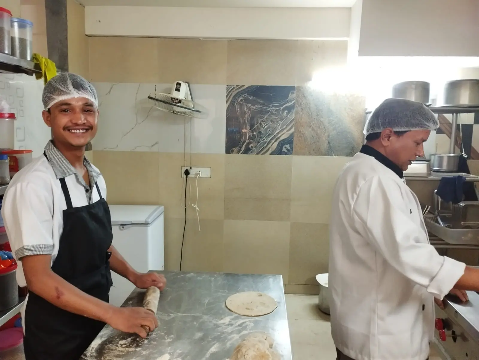 Two Commune chefs rolling and cooking rotis in the kitchen