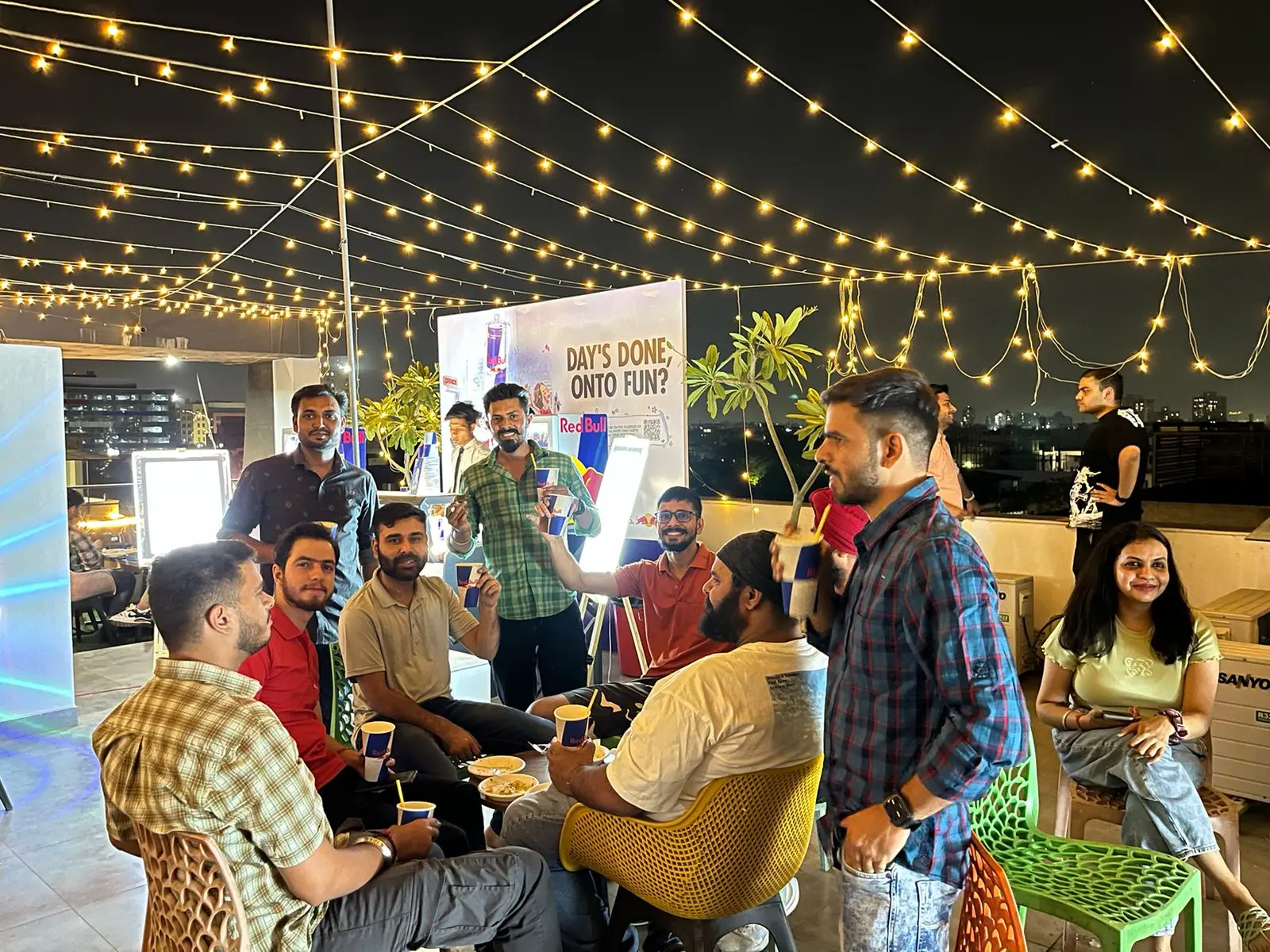 Communrs raising their cups together under string lights on a Commune rooftop at night