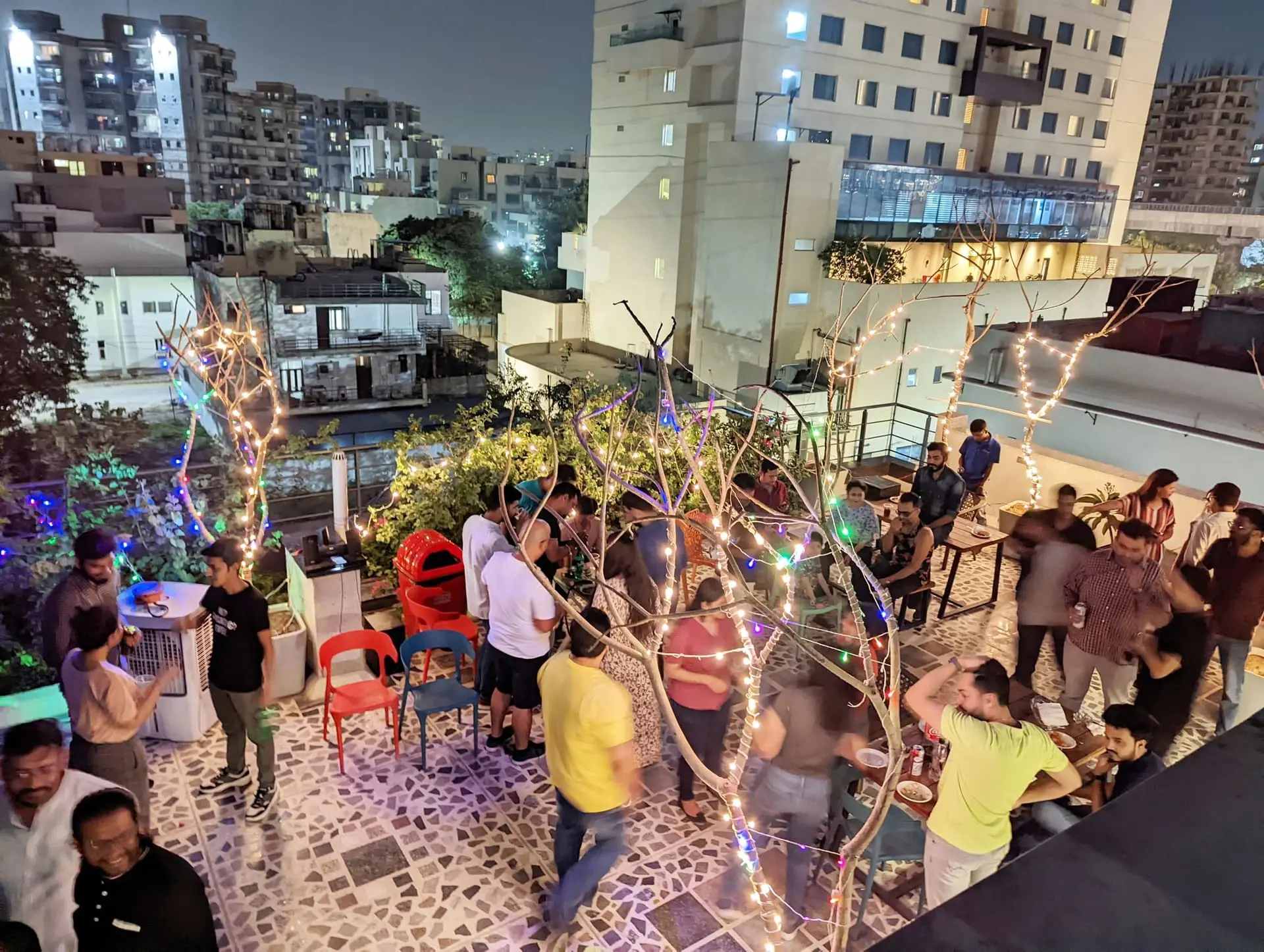 Communrs at a party on the rooftop terrace, city lights behind