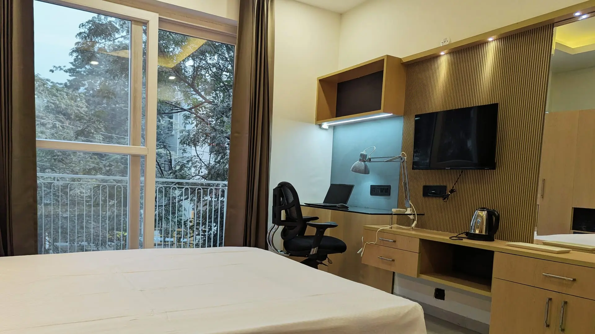 A furnished Commune room with a desk, TV and a view of the trees